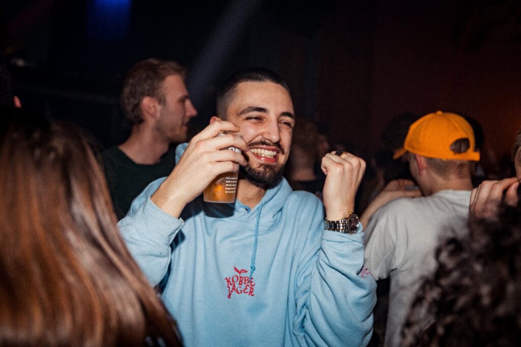 Bezoeker van het hip hop evenement Trillers, in Gent - De jongen draagt een blauwe trui met rode letters en is gelukkig aan het feesten met een pint in de hand - Hij is omringd door een aantal andere jongens en meisjes